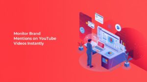 An isometric illustration on a vibrant red background showing a person working at a desk with multiple floating monitors, accompanied by the text "Monitor Brand Mentions on YouTube Videos Instantly."